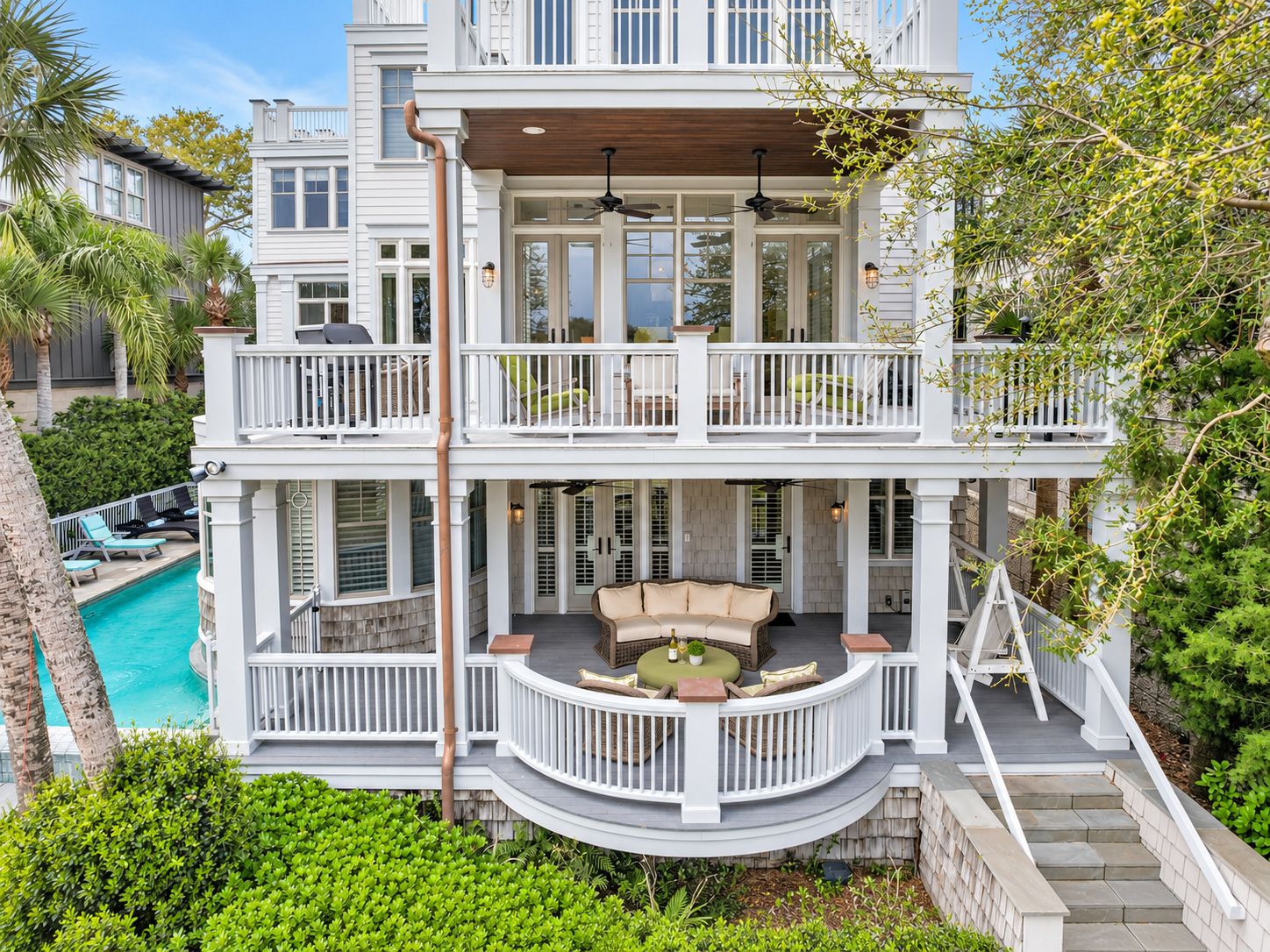 A two-story house with a balcony, a pool, and a patio with outdoor furniture.