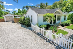A single-story house with a gravel driveway, a white picket fence, and a well-maintained lawn.