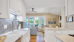 Una cocina moderna con armarios blancos, lavavajillas integrado y un amplio ventanal con vistas a un jardín.