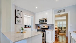 Una cocina moderna con armarios blancos, una isla central, electrodomésticos de acero inoxidable y vistas al salón.