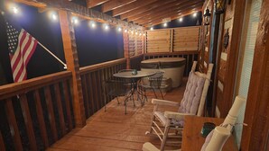 A wooden deck with a table and chairs, a cushioned chair, and an American flag. - Family friendly rustic cabin tucked away, just minutes from entertainment! (Sevierville)