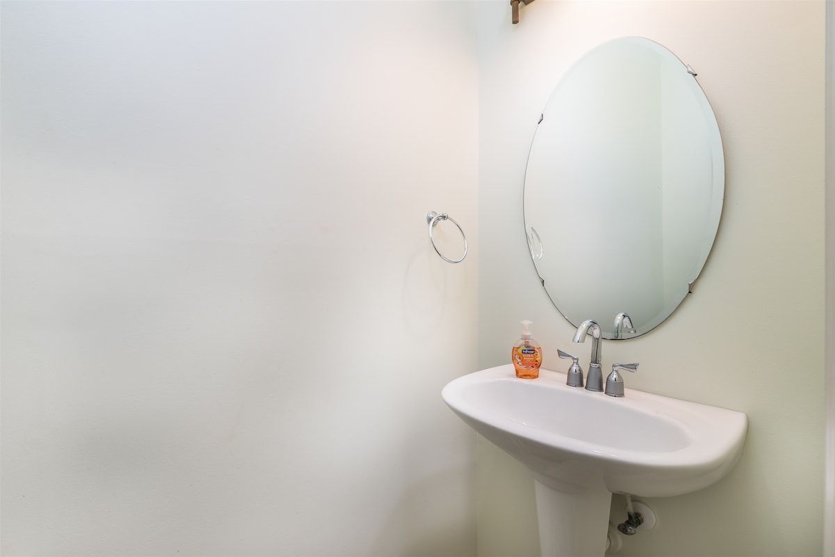 Un baño con un lavamanos blanco, un espejo redondo y un dispensador de jabón.