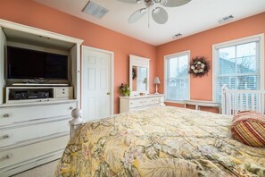 Une chambre à coucher comprenant un lit, une commode, un téléviseur et un ventilateur de plafond.