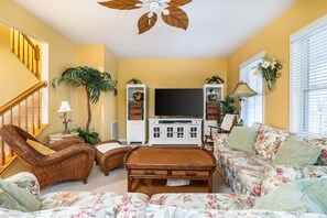A living room with a television, wicker furniture, a sofa, and a ceiling fan.