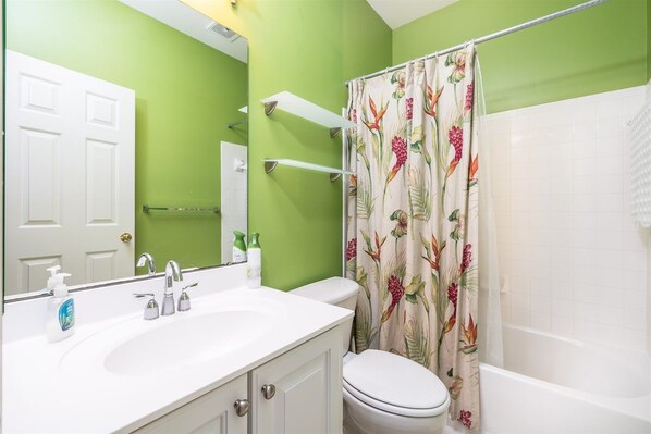 Un baño con lavamanos, inodoro y bañera blancos. Hay una cortina de ducha con estampado floral.