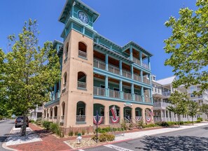 A multi-story building with a clock tower, balconies, and American flags. - Sunset Island 30 Island Edge Drive (Ocean City)