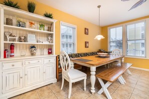 A dining area with a wooden table, white chairs, a bench, and a white cabinet with shelves.