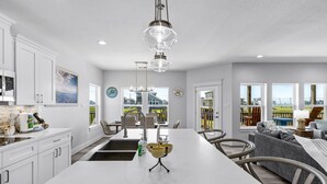 Una cocina moderna con armarios blancos, una isla grande y un comedor con un sofá y sillas grises.