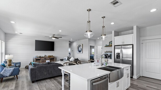 Una cocina moderna con una isla central, electrodomésticos de acero inoxidable y un área de comedor con un sofá gris.