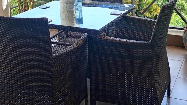Un espace extérieur aménagé, abrité et doté d'une table et de chaises en osier, offrant une vue sur un plan d'eau et la verdure environnante.