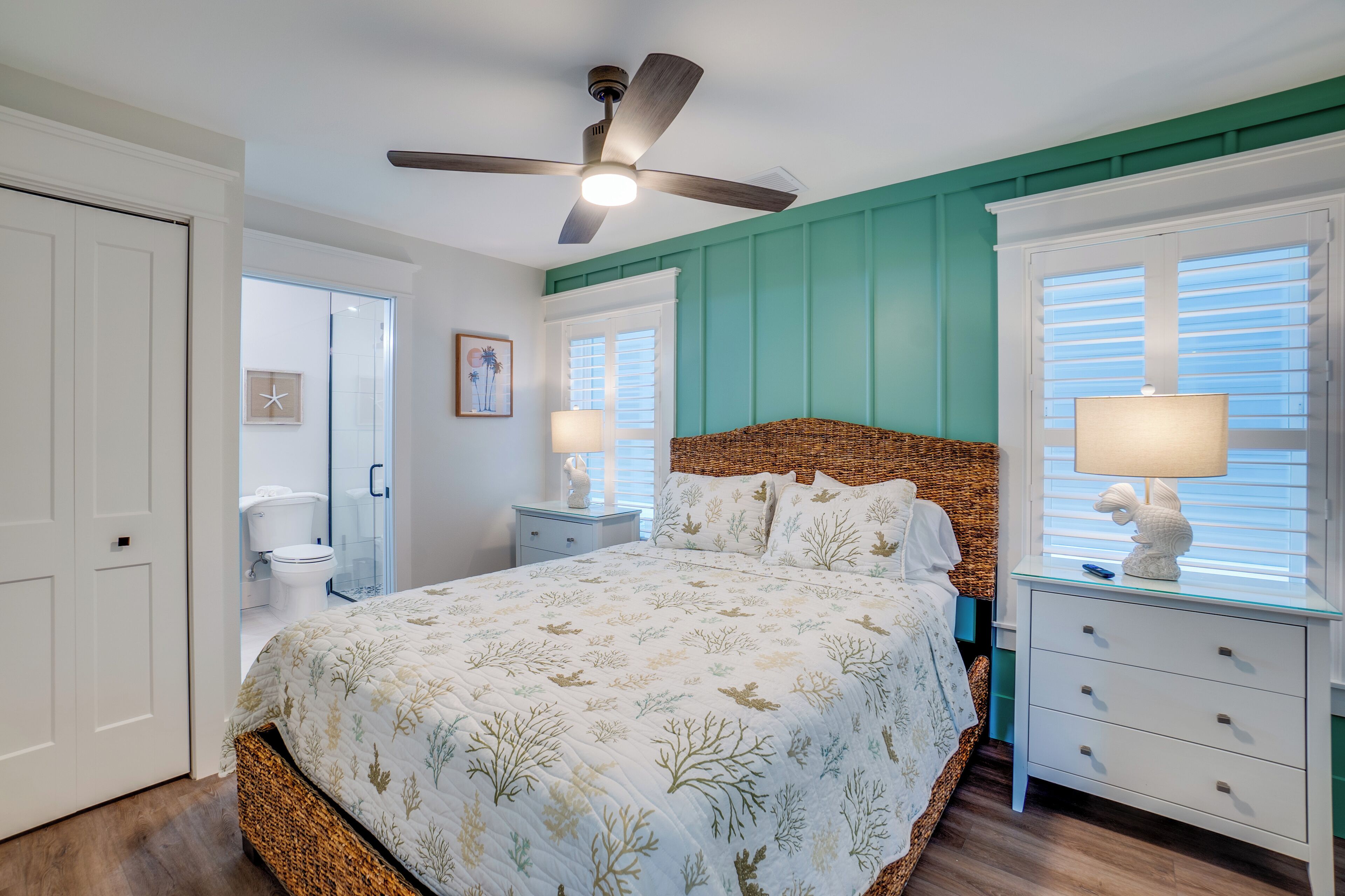 A bedroom with a bed, a nightstand, a dresser, a ceiling fan, and a window with shutters.