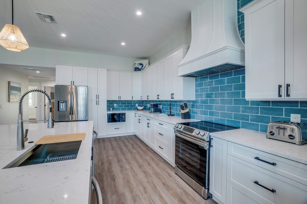 A modern kitchen with white cabinetry, a blue tiled backsplash, stainless steel appliances, and a built-in oven.