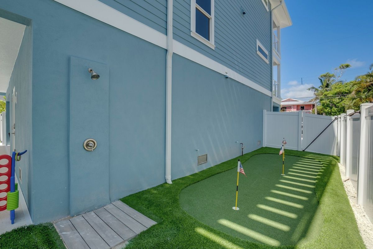 Una propiedad residencial con fachada azul, un pequeño césped artificial verde y una valla blanca.