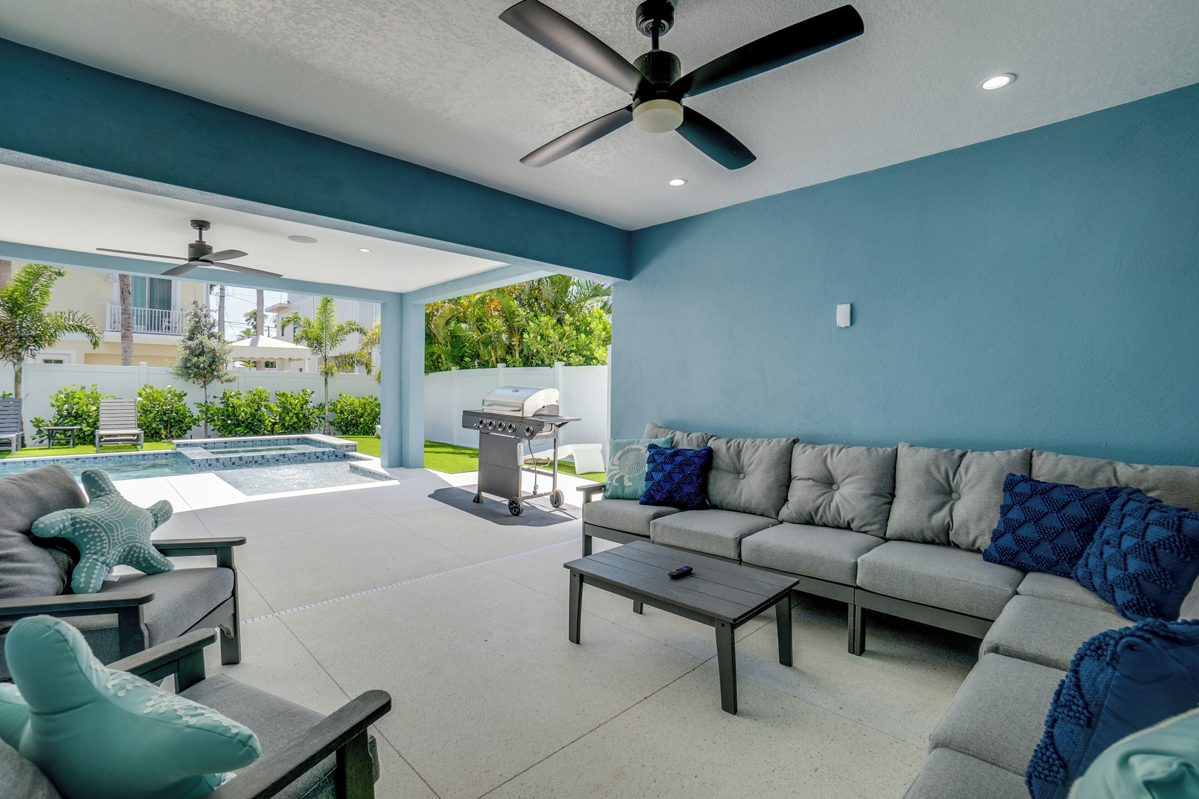A modern outdoor living area with a gray sofa, a coffee table, and a ceiling fan.