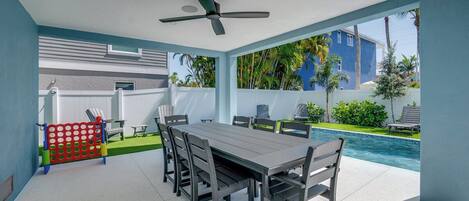 A covered outdoor dining area with a pool view, a ceiling fan, and a red and blue play structure.