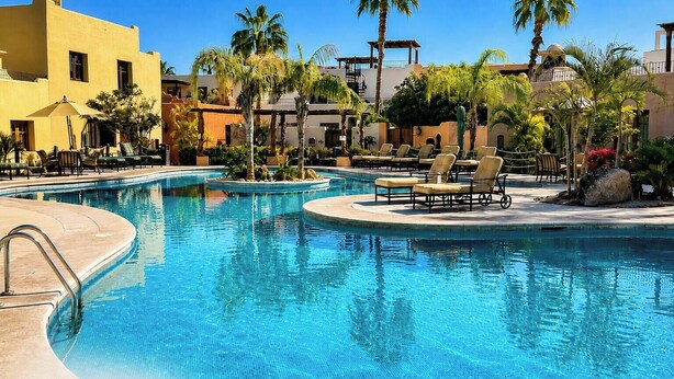 Un área de piscina con sillas de descanso y palmeras.