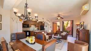 Amplia sala de estar con una mesa de comedor lista para cuatro comensales, una cocina equipada con electrodomésticos modernos y una zona de estar acogedora con sofá y sillones.