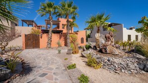 Un patio con un sendero de piedra, palmeras y un edificio con puerta de madera.