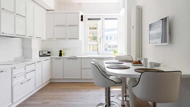 A modern kitchen with white cabinets, a dining table with chairs, and a window with a view of buildings. - Pure White - My Home in Como (Como)