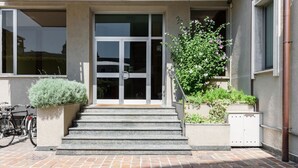 A building entrance with a glass door, steps, a bicycle, and potted plants. - Pure White - My Home in Como (Como)