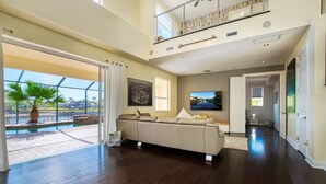 Una sala de estar amplia con un sofá grande, vistas a la piscina y una escalera que sube a un nivel superior.