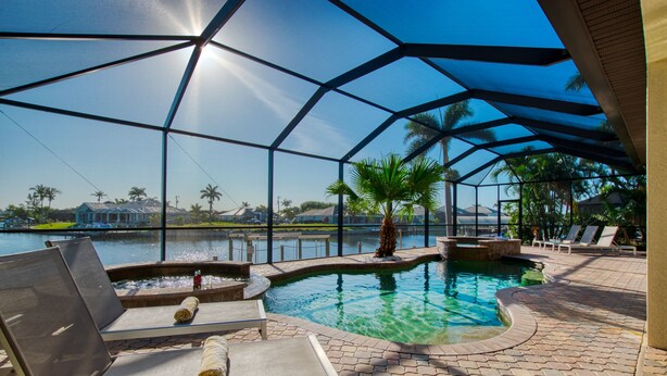 Un área de piscina con sillones de descanso, una fuente de agua y vistas a un cuerpo de agua y palmeras.
