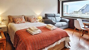Een moderne hotelkamer met een groot bed, een sofa, een eethoek en uitzicht op de stadsgezicht.