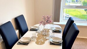 A dining area with a white table, black chairs, and a vase with pink flowers. - Private Parking, Urban Comfort & City Haven (Plymouth)