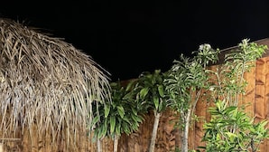 Un espacio al aire libre con mobiliario de mimbre y techo de paja, rodeado de paredes de madera y plantas tropicales.
