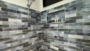 Zona de ducha con pared de azulejos, ducha y repisa con artículos de aseo.