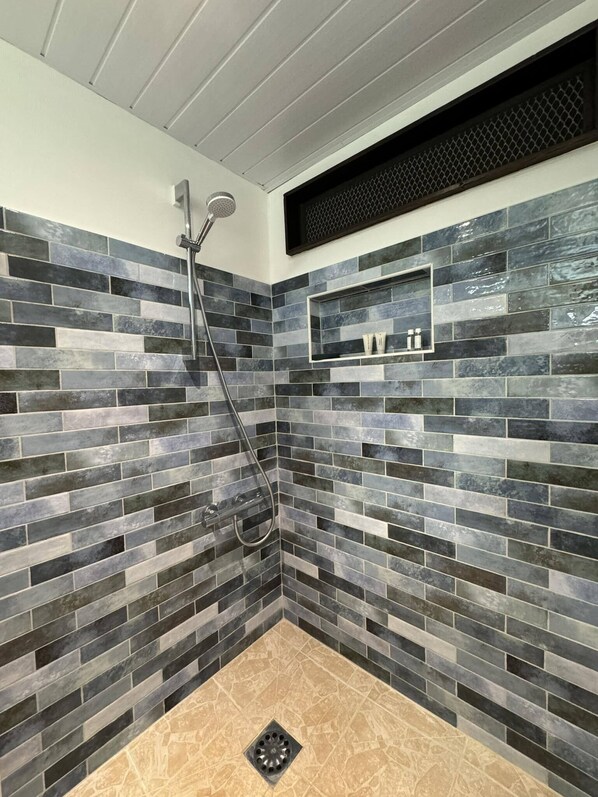Un espace douche avec un mur carrelé, une pomme de douche et une étagère contenant des articles de toilette.