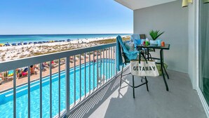 Un balcone con piscina, vista sulla spiaggia e un tavolo con una borsa 'GETAWAY'.