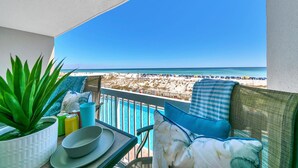 Un balcone con vista sulla spiaggia, una sedia, un tavolo con una ciotola e una pianta, e un cuscino blu.