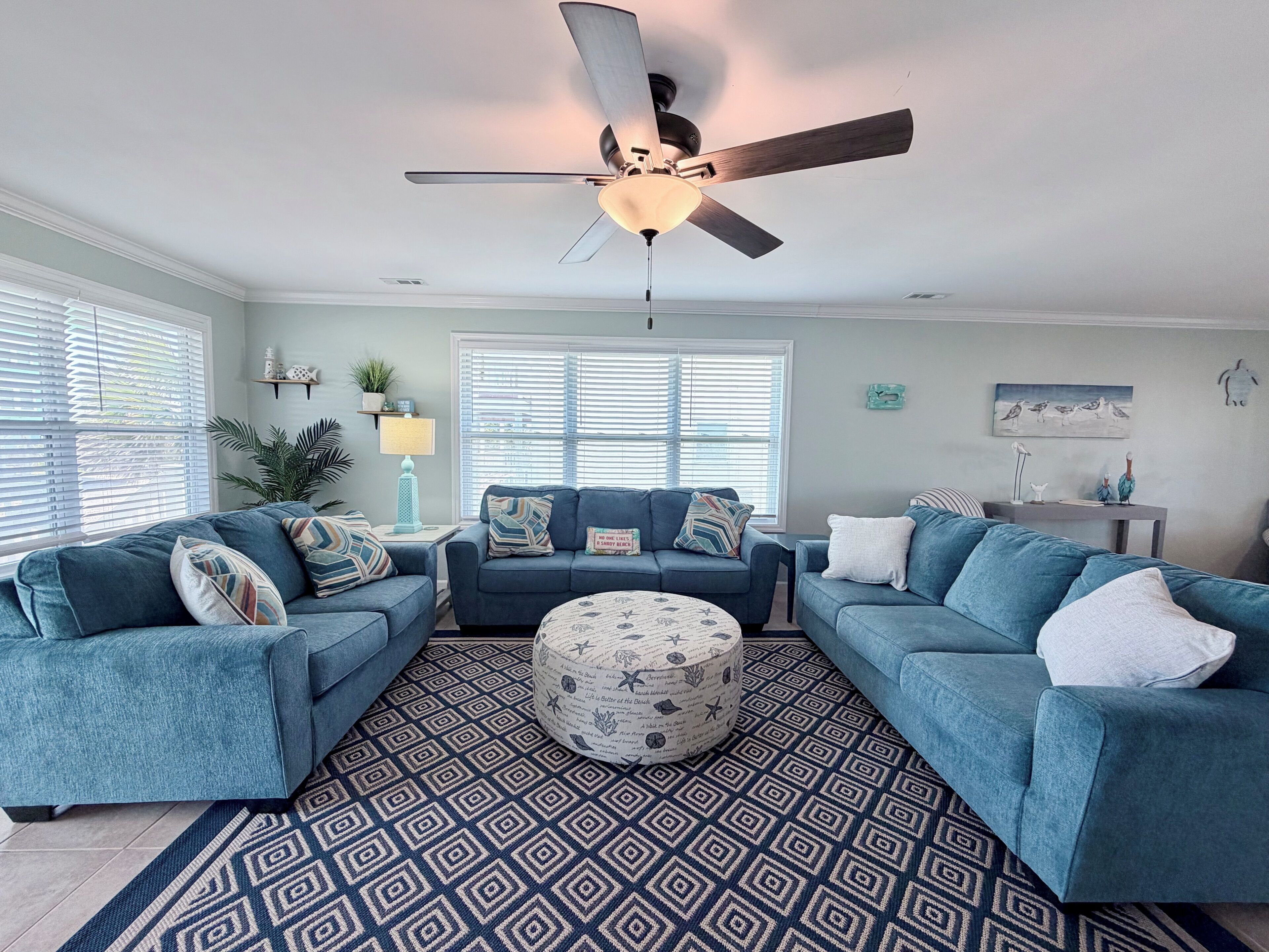 A living room with a ceiling fan, two sofas, a patterned rug, and a window with blinds.