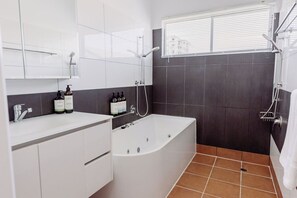 Un baño moderno con bañera, ducha y tocador con artículos de aseo.