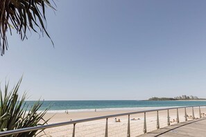 Ein Strand mit einer Holzpromenade, Palmen und einer entfernten Skyline.