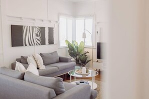 Un salon moderne avec un canapé gris, une table basse ronde, une grande plante et un téléviseur.