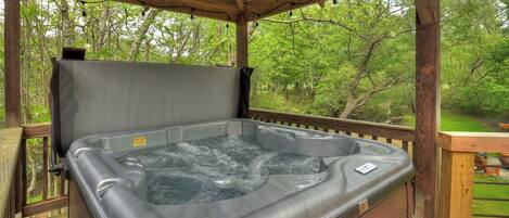 A hot tub under a wooden pergola with a view of a forested area.
