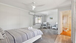 Un dormitorio con cama, dos sillas, una mesita, una ventana y un rincón de ducha.