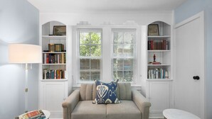 A cozy room with a sofa, a small table, and a bookshelf filled with books. - Forest Hills Manor w/ King Bed (Augusta)