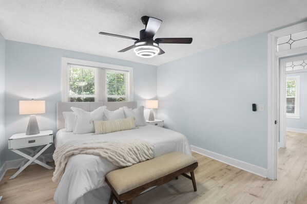 A bedroom with a bed, bedside tables, a bench, a ceiling fan, and a window with blinds.