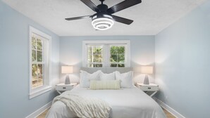 A bedroom with a bed, two bedside tables, a ceiling fan, and two windows with blinds. - Forest Hills Manor w/ King Bed (Augusta)