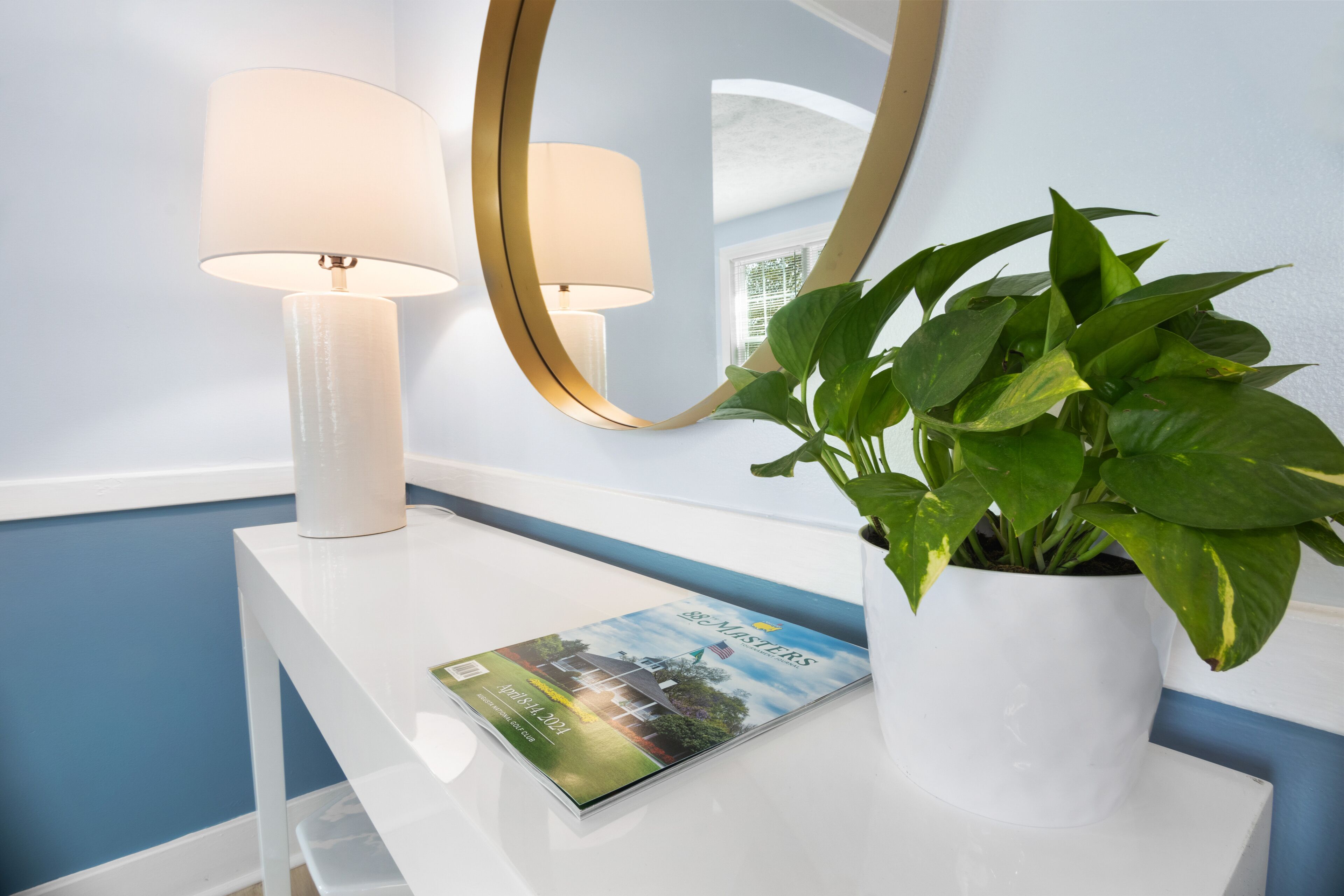 A white console table with a magazine, a potted plant, and two lamps.