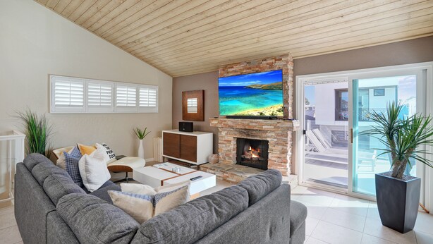 Uma sala de estar moderna com lareira de pedra, uma televisão de tela grande e um sofá cinza.