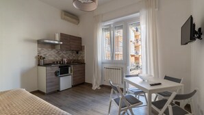 Eine kompakte Küche mit Herd, Spüle und Schränken, ein Essbereich mit Tisch und Stühlen sowie ein großes Fenster mit Vorhängen.