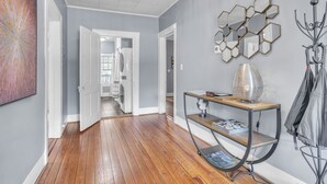 Un couloir doté d’un plancher en bois, d’un porte-manteau, d’un mur décoré de miroirs et d’une porte donnant sur une buanderie.