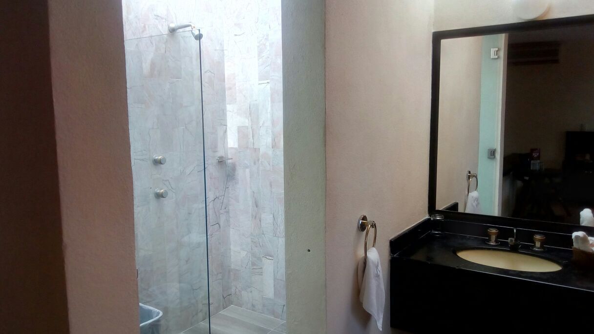 A bathroom with a glass shower enclosure, a sink with a mirror, and a towel hanging on the wall.
