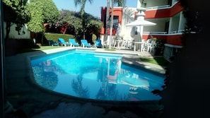 A swimming pool with blue water, surrounded by lounge chairs and a building with red and white exterior. - Hotel Real del Sol Cuernavaca (Cuernavaca)