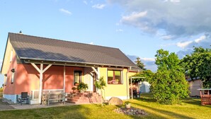 A two-story house with a sloped roof, a front porch, and a small garden area with a bench and potted plants. - Zum Koppelblick by Interhome (Woldegk)