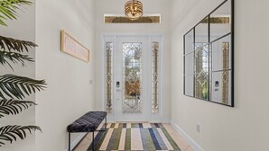 Un couloir avec un banc, une porte ornée de vitraux et un miroir fixé au mur.